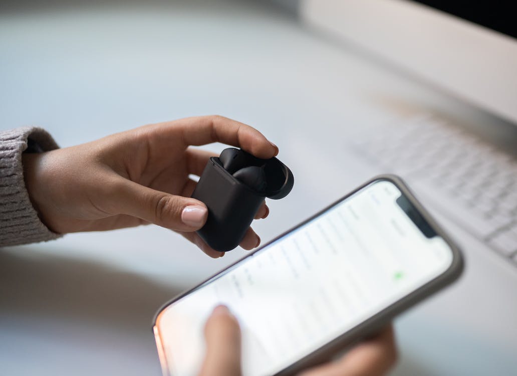 Person holding wireless earphones next to a smartphone, ready to start listening with a text to voice app